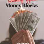 A digital cover for the Busting Your Money Blocks Workbook from Shifting To Abundance. The image shows a woman holding a fan of hundred-dollar bills with the top edges dramatically on fire, symbolizing the release of limiting beliefs about money. Bold text highlights the workbook’s title in red and black, with “WORKBOOK” in all caps at the bottom, reinforcing the focus on transforming money mindset and attracting financial freedom.